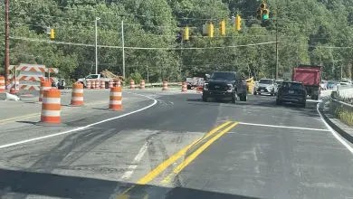 Vehicles moving through the N.C. 105 and Broadstone Road intersection on a green signal, with barricades closing the old bridge alignment at left.