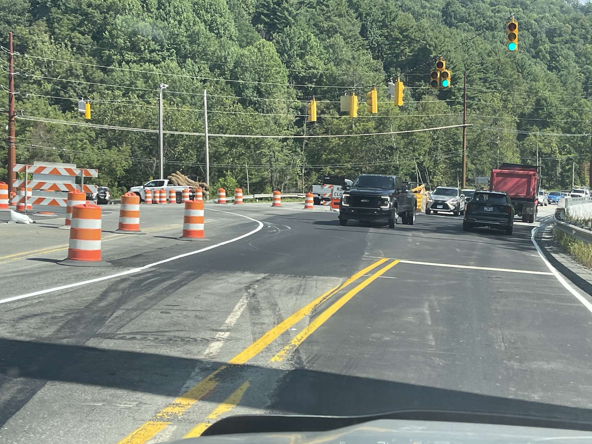 Vehicles moving through the N.C. 105 and Broadstone Road intersection on a green signal, with barricades closing the old bridge alignment at left.