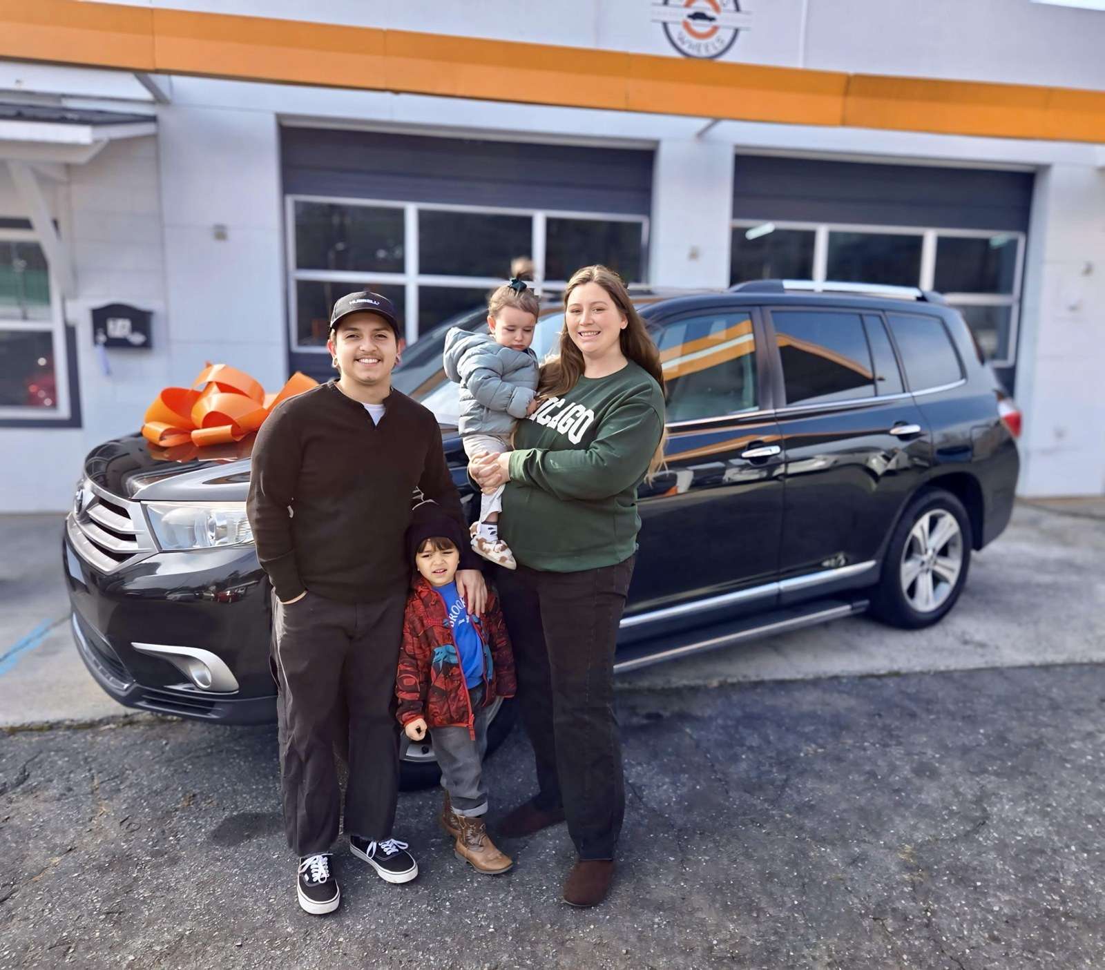 A family stands with their vehicle in front of the Working Wheels shop