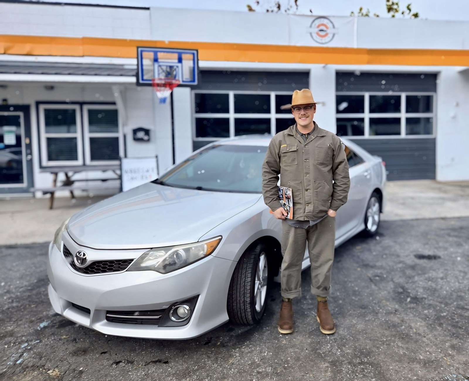 A man stands beside a silver car in front of the Working Wheels shop